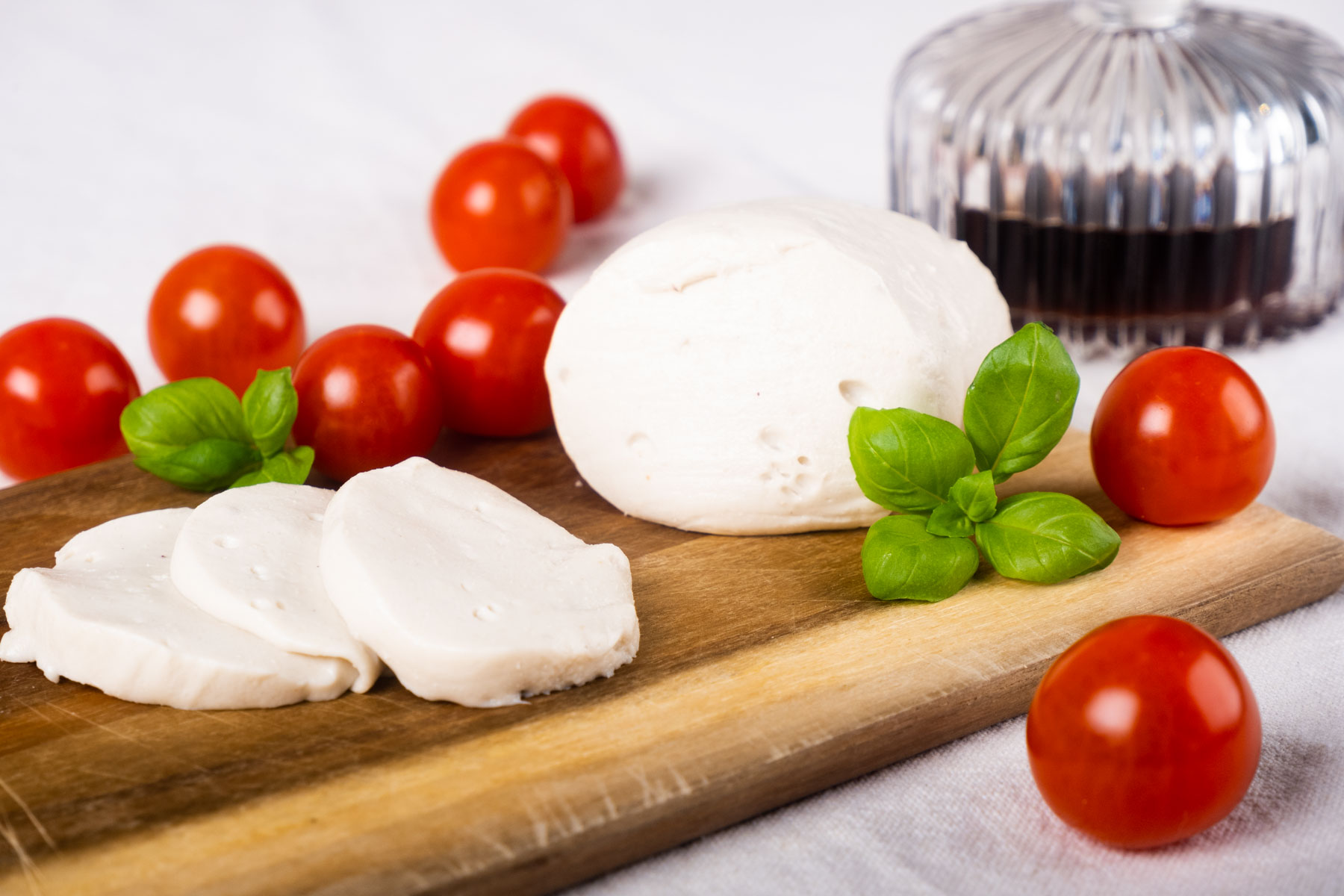 Veganer Mozzarella auf Cashew-Basis mit Cherrytomaten und Basilikum auf einem Holzbrett VANOZZA foods